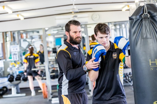 male student with male teacher being taught how to use boxing bag