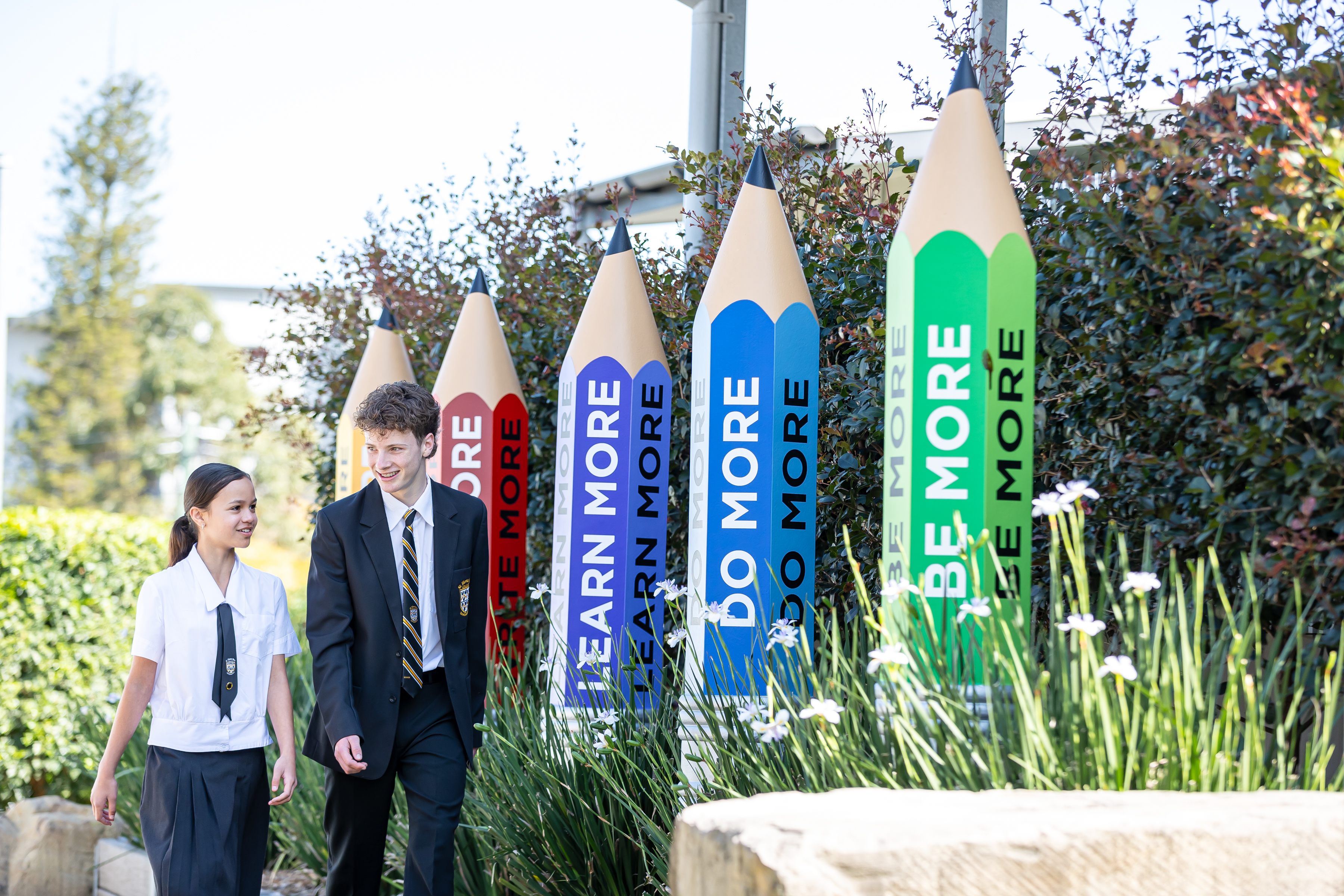Students walking past STMC Pencils with College Mottos