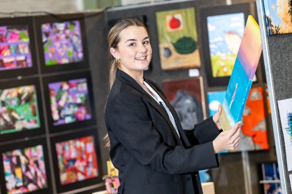 student presenting artwork in an exhibition setting, highlighting achievement, confidence and artistic expression
