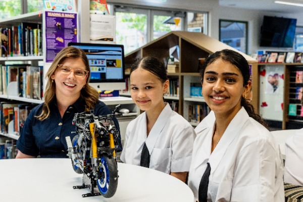 teacher and students working together on a robotics model in a library setting, reflecting hands on STEM learning, collaboration and innovation