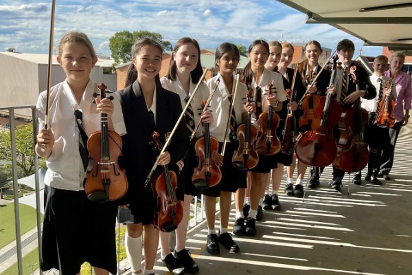 students holding string instruments together on a school walkway, representing music ensemble participation, collaboration and performance opportunities