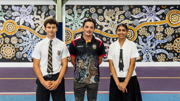 students standing with staff member in front of large Aboriginal mural artwork indoors