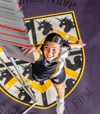 student reaching upward beneath the college crest in a dynamic pose, representing aspiration, energy and school pride