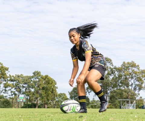 student placing a rugby ball on the ground to take a kick, reflecting skill development, focus and engagement in sport