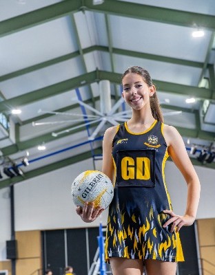 student in netball uniform holding a ball on an indoor court, highlighting participation, development and pride in school sport