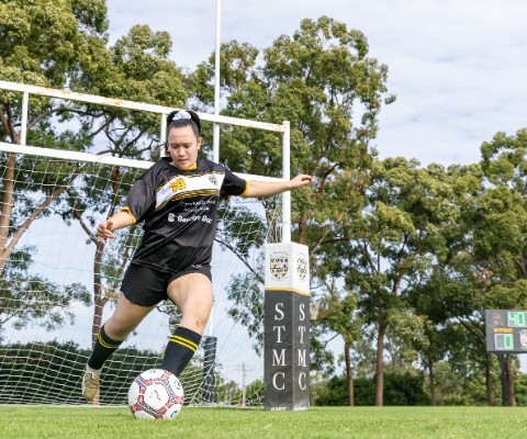 student kicking a soccer ball near the goal posts during play, highlighting coordination, technique and active participation in sport