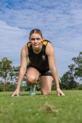 student in athletic uniform crouched on grass ready to sprint, representing physical readiness, determination and school sport participation