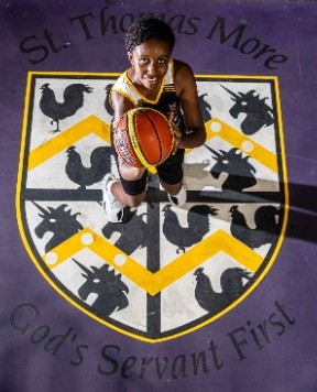 student holding a basketball while standing over the college crest on a court, representing school pride, identity and participation in sport
