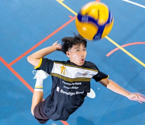 student jumping to spike a volleyball during indoor play, highlighting strength, timing and participation in school sport