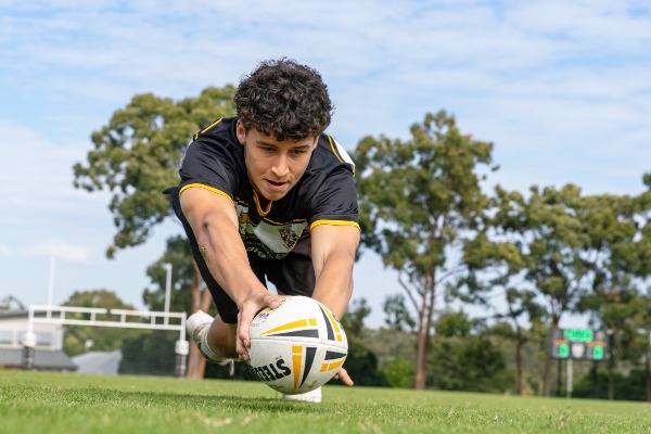 student diving forward with a rugby ball during play, highlighting commitment, skill and competitive participation