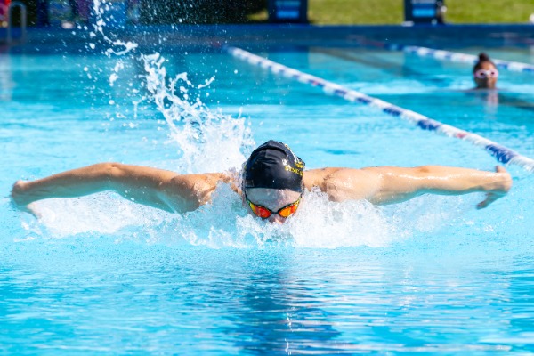 student performing butterfly stroke during a swim race, reflecting strength, technique and school sport participation