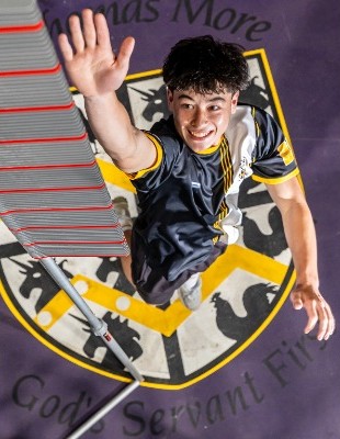 student reaching upward beneath the college crest in a dynamic pose, representing energy, aspiration and school pride