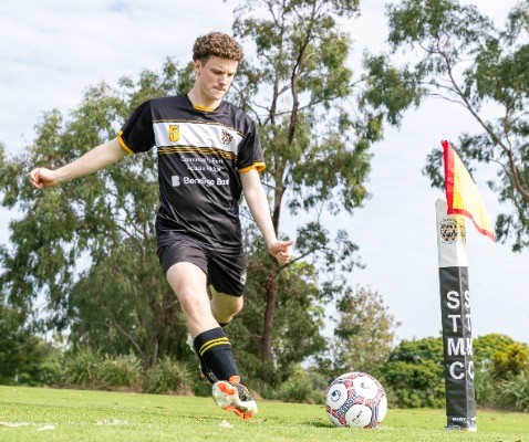 student striking a soccer ball near a corner flag on the field, reflecting skill, focus and competitive play