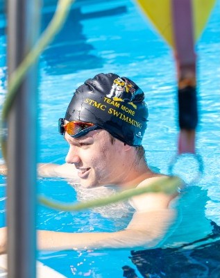 student resting at the pool wearing team swim cap, reflecting participation, recovery and school swimming program