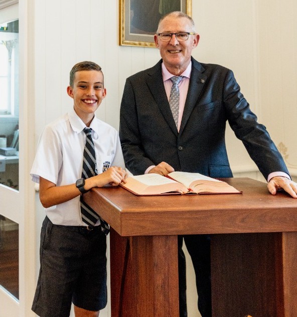 student and principal standing at a lectern with an open book, representing leadership, mentoring and student voice