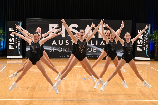 students performing a synchronised aerobics routine on an indoor court, highlighting teamwork, coordination and participation in competitive school sport