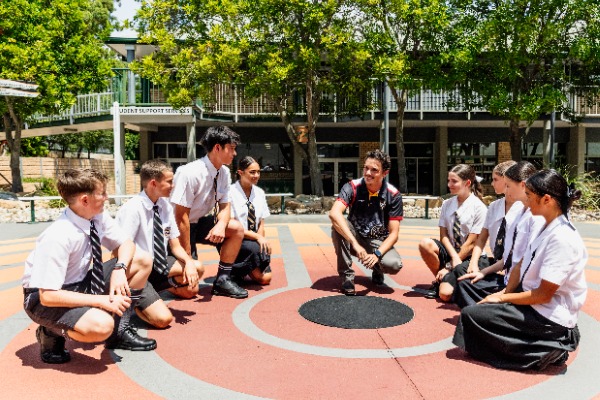 students sitting in circle on school courtyard ground with staff member leading discussion outdoors