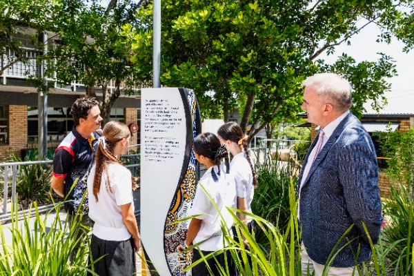 students gathered around staff member reading outdoor cultural display sign surrounded by greenery