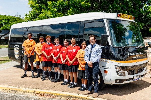 students lined up with a staff member in front of a school bus, representing transport services, safety and access to school community activities