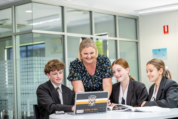 teacher guiding students working together on a laptop in a collaborative classroom setting, reflecting support, engagement and focused learning